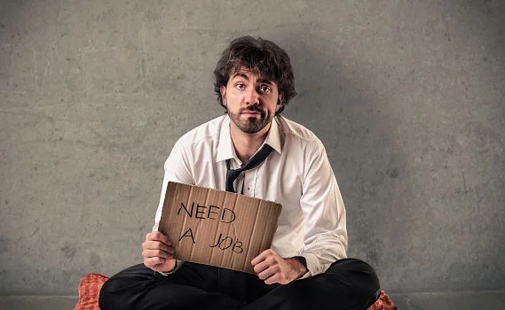 уволенный офисный работник сидит с плакатом need a job