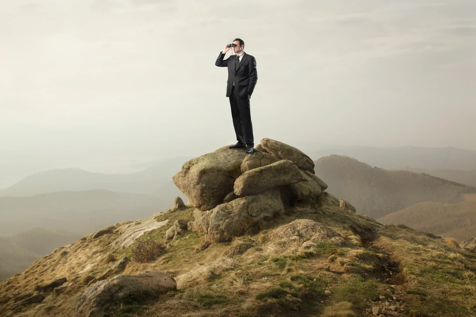мужчина в костюме на горном холме смотрит в бинокль