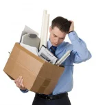 молодой человек держит коробку с офисными принадлежностями и задумчиво держит рукой голову