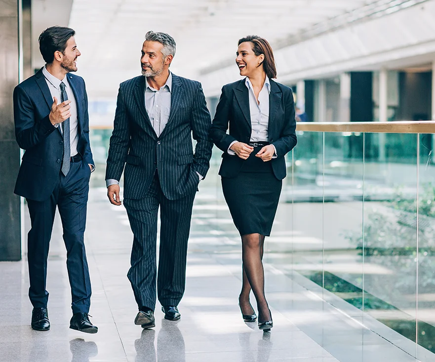 топ менеджер и два менеджера оживленно беседут проходя вдоль стеклянных перил здания