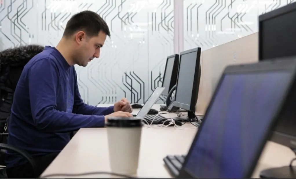 молодой человек сосредоточенно работает за ноутбуком в офисе