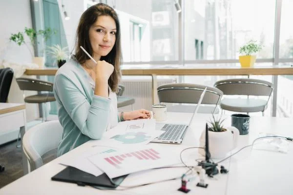 Девушка администратор сидит за столом с ноутбуком и документами в офисе