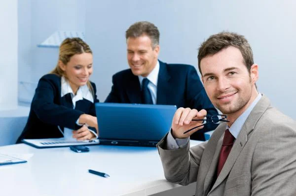 Мужчина аккаунт-менеджер держит очки и сидит за столом с сотрудниками