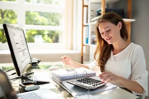 Девушка бухгалтер на первичную документацию работает с калькулятором, папкой и компьютером и держит ручку