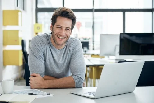 Мужчина DevOps-инженер сидит за столом с ноутбуком в офисе