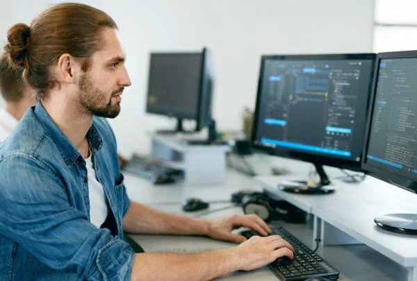 Мужчина frontend разработчик пишет код на компьютере с двумя мониторами