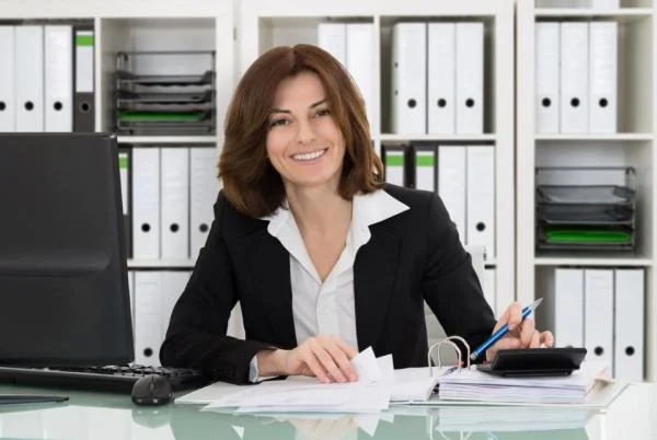 Женщина главный бухгалтер сидит за столом с документами, калькулятором и ручкой