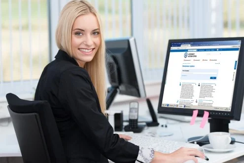 Девушка главный бухгалтер сидит обернувшись за столом и работает за компьютером