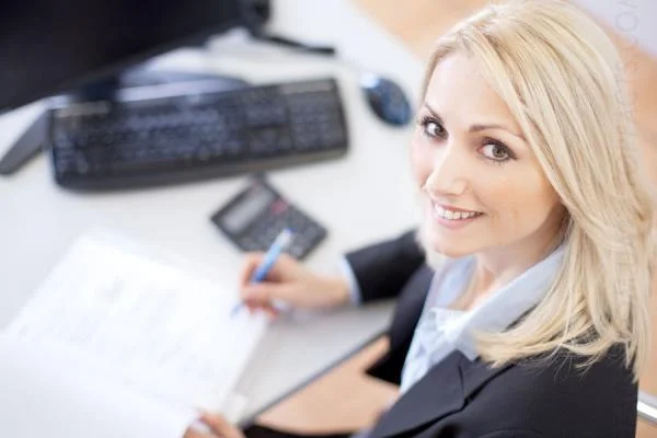 Девушка главный бухгалтер сидит за столом и делает запись в журнал