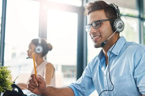 Мужчина инженер по поддержке в очках общается через гарнитуру в офисе и держит ручку