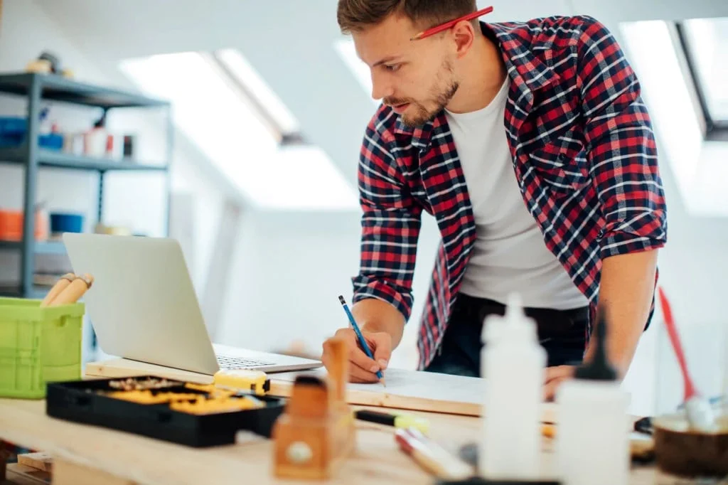 Мужчина инженер-проектировщик делает запись с ноутбука в чертеж