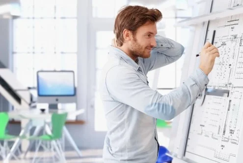 Мужчина инженер-проектировщик холодильного оборудования работает с чертежом в офисе на фоне стола и компьютера