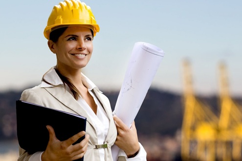 Девушка инженер-сметчик в желтой каске держит чертеж и планшет