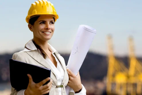 Девушка инженер-сметчик в каске держит папку и чертеж на фоне стройки