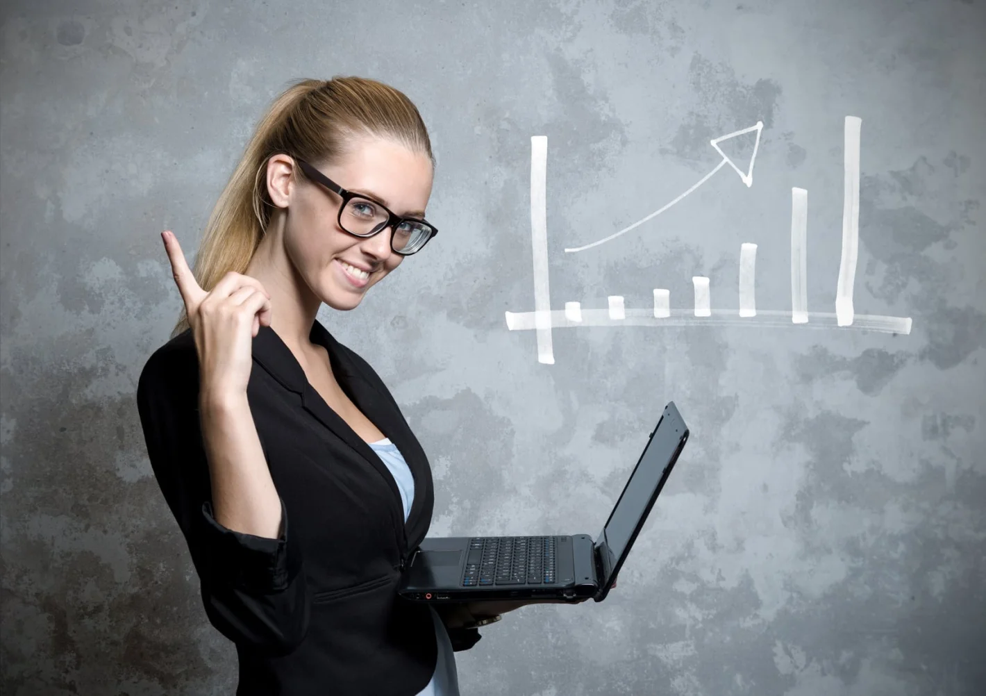Девушка маркетолог в очках стоит на фоне графика и держит в руке ноутбук