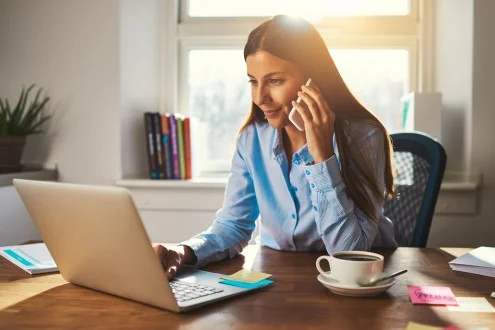 Девушка маркетолог сидит с телефоном и ноутбуком за столом офисе