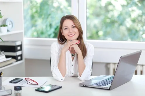 Девушка менеджер по персоналу сидит за столом с ноутбуком, планшетом и телефоном