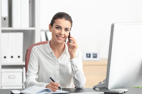 Девушка менеджер по по продажам мембранных тканей сидит за столом в офисе, разговаривает по телефону и держит ручку