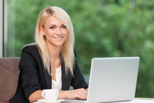 Молодая менеджер по продажам сидит с чашкой и ноутбуком на фоне деревьев