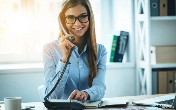 Девушка менеджер по развитию сидит за столом в офисе и набирает номер на телефоне
