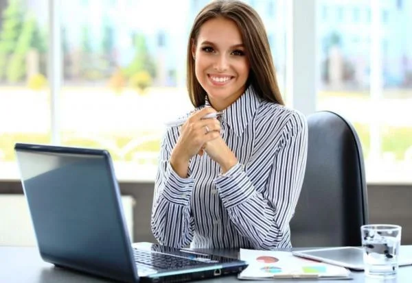 Девушка менеджер по продажам сидит за столом с ноутбуком, графиками и стаканом воды