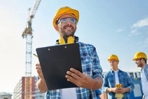 Мужчина начальник участка стоит на фоне стройки и сотрудников и держит в руках документацию