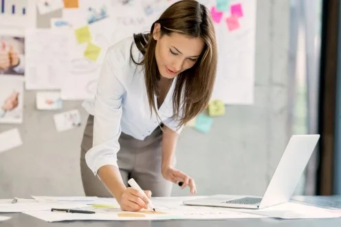 Девушка продакт-менеджер делает пометку маркером за столом с ноутбуком