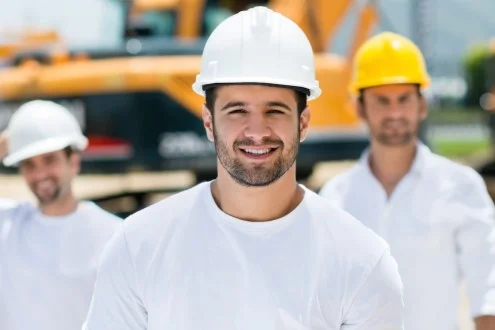 Мужчина прораб / начальник участка в белой каске на фоне сотрудников и строительной техники