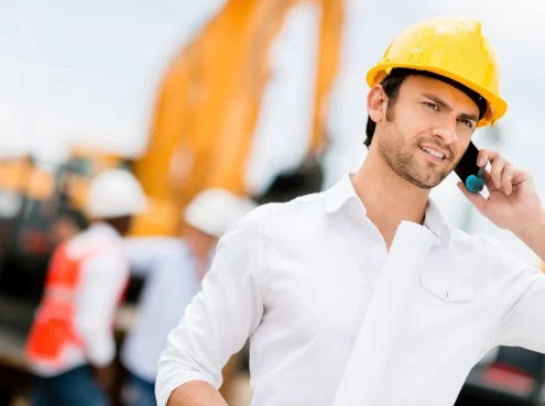 Мужчина прораб в каске с телефоном на строительной площадке вместе с рабочими