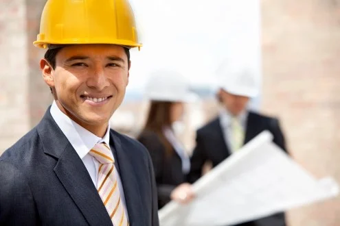 Мужчина руководитель строительных проектов в каске стоит на фоне сотрудников, изучающих чертеж