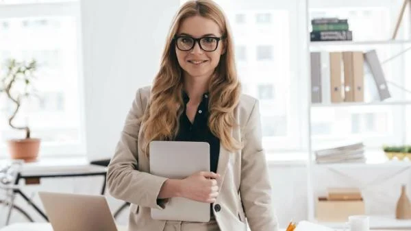 Девушка специалист по казначейскому сопровождению в очках и пиджаке в офисе держит планшет