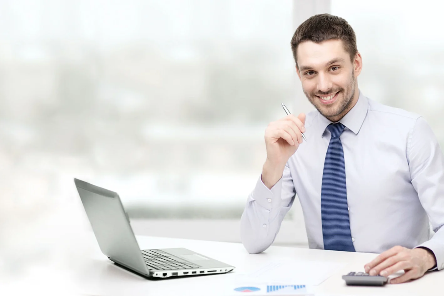 Мужчина специалист по тендерам сидит с ручкой за столом с калькулятором и ноутбуком