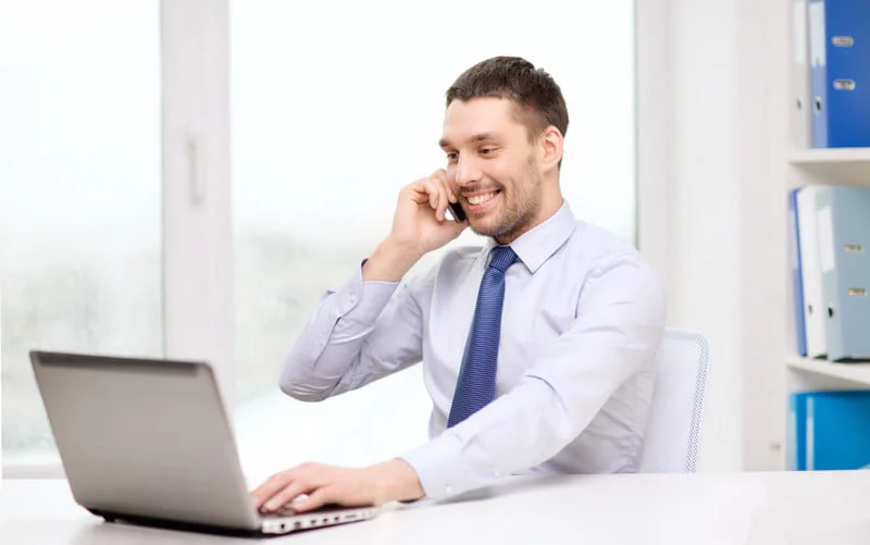 Мужчина специалист по закупкам разговаривает по телефону и смотрит на экран ноутбука