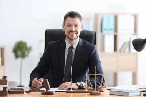 Мужчина судебный юрист в пиджаке сидит в креселе за столом с весами и молотком и держит ручку