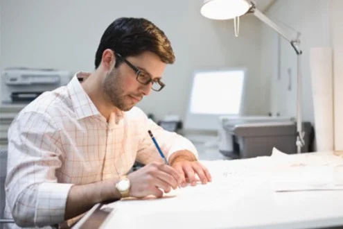 Мужчина инженер конструктор работает с чертежом за столом