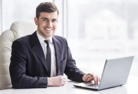 Мужчина менеджер по продажам сидит за столом с ноутбуком в белом кресле