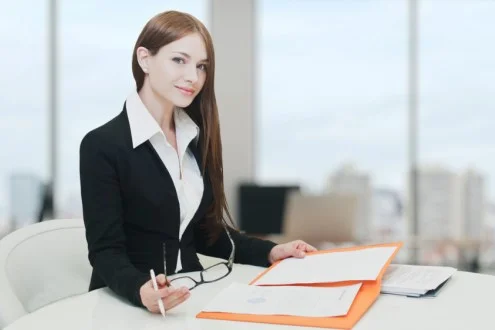 Девушка юрист сидит за столом в офисе и держит документы и очки