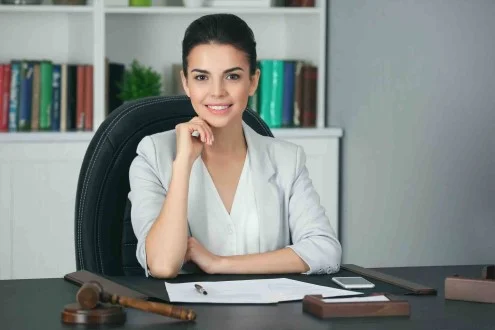 Девушка юрист в единственном лице сидит за столом в офисе с документами, телефоном, ручкой и деревянным молотком