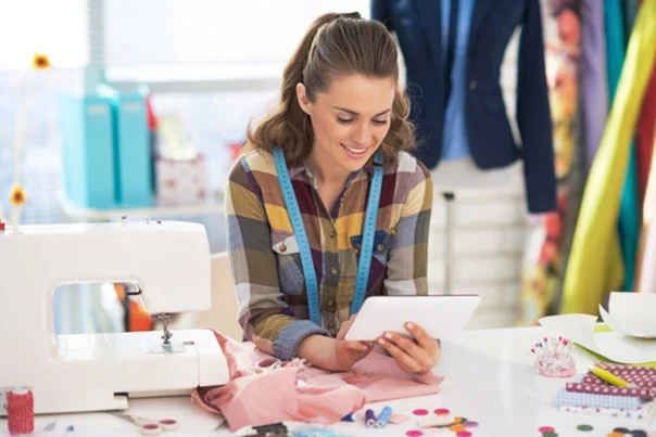 Девушка помощник менеджера по закупкам за столом с планшетом швейной машинкой и одеждой